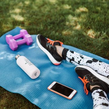Focused workout setup outdoors with mat, dumbbells, phone, and water bottle.